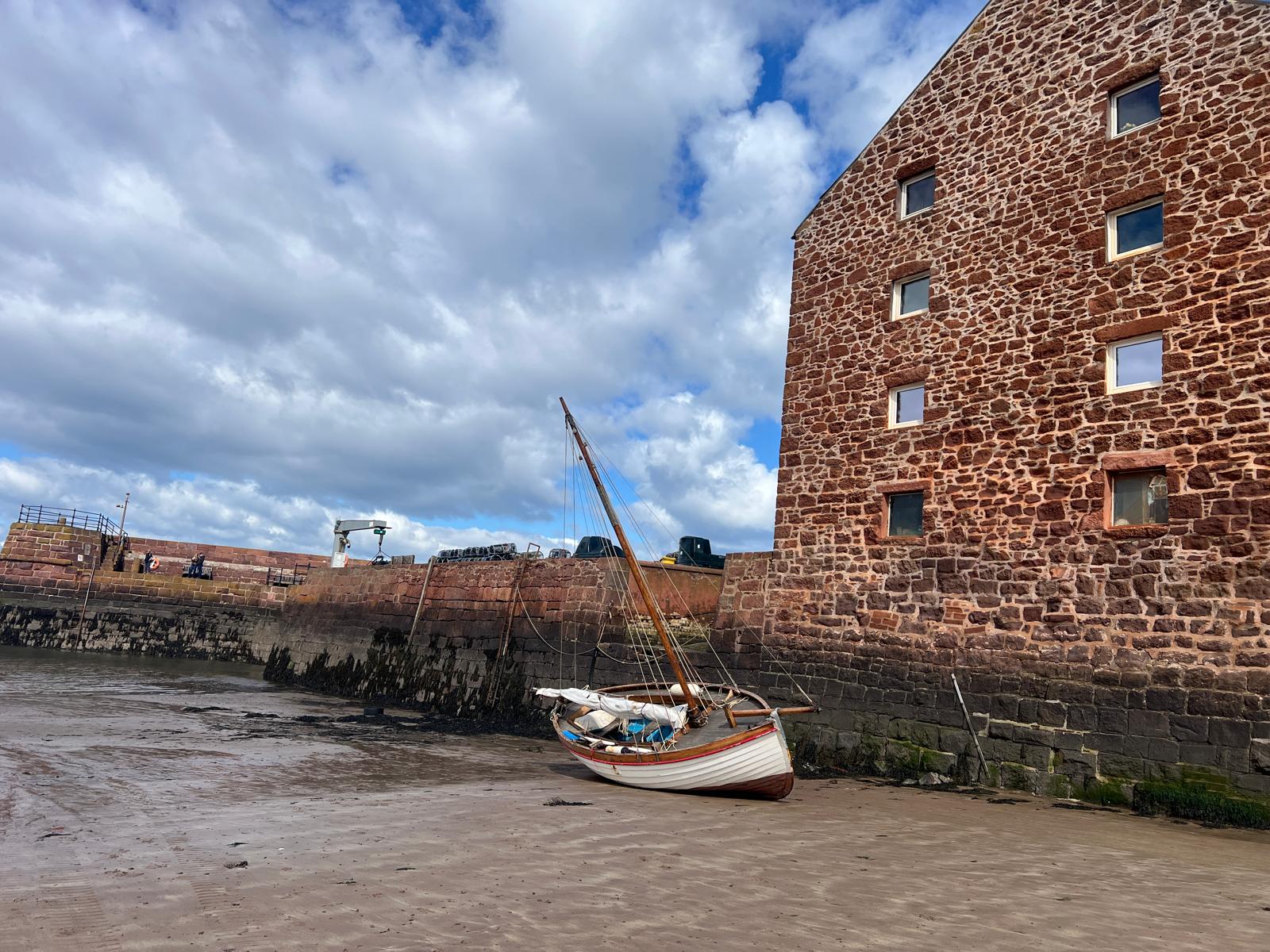 A small boat aground on the sand at low tide beside a harbour wall